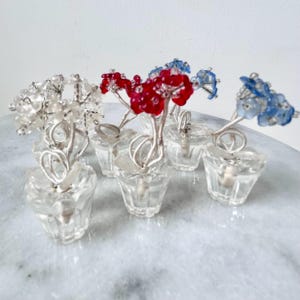 May include: Six miniature glass flower pots with wire stems and beaded flowers. The flowers are white, red, and blue.