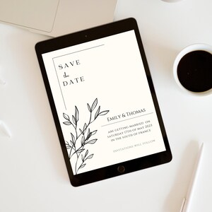 May include: A white digital tablet with a black border displays a save the date announcement for Emily & Thomas. The announcement features a simple black and white floral design and the text "Save the Date" and "Emily & Thomas are getting married on Saturday 17th of May 2023 in the South of France. Invitations will follow."