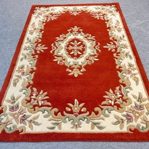 May include: A red rug with a cream-colored border featuring a floral pattern. The rug has a central medallion with a floral design.