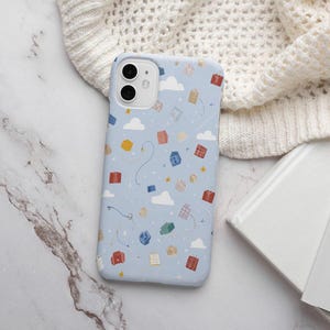 May include: A light blue phone case with a pattern of colorful gift boxes, clouds, and stars. The case has a smooth finish and is designed for a smartphone. The case is lying on a white knitted surface.