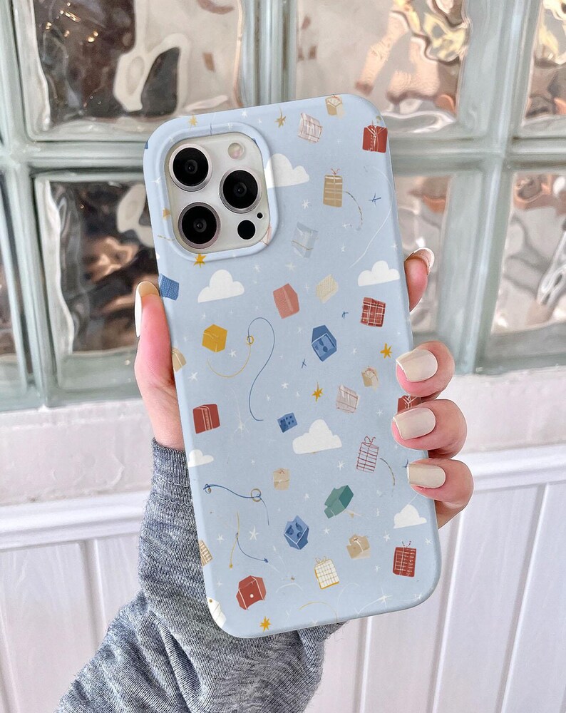 May include: A light blue phone case featuring a pattern of colorful gift boxes, white clouds, and gold stars. The case has a smooth finish and a camera cutout. The design includes whimsical lines and dots.
