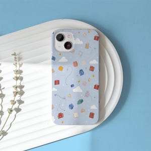 May include: A light blue phone case with a whimsical pattern of floating gift boxes, clouds, and stars. The case has a glossy finish and a camera cutout. The design includes red, yellow, and blue gift boxes.