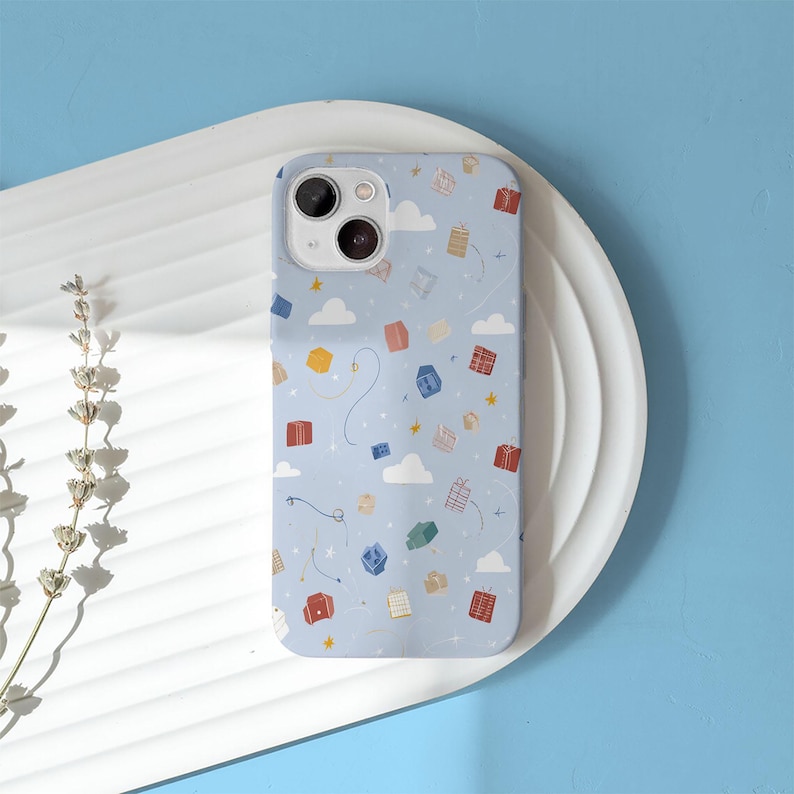 May include: A light blue phone case with a whimsical pattern of floating gift boxes, clouds, and stars. The case has a glossy finish and a camera cutout. The design includes red, yellow, and blue gift boxes.