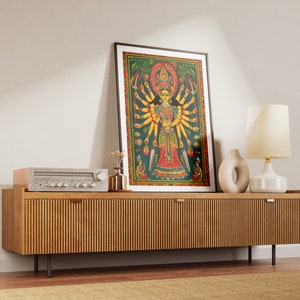 May include: A framed print of a colorful painting depicting a Hindu deity with multiple arms. The print is displayed on a wooden cabinet with a stereo system and a lamp.