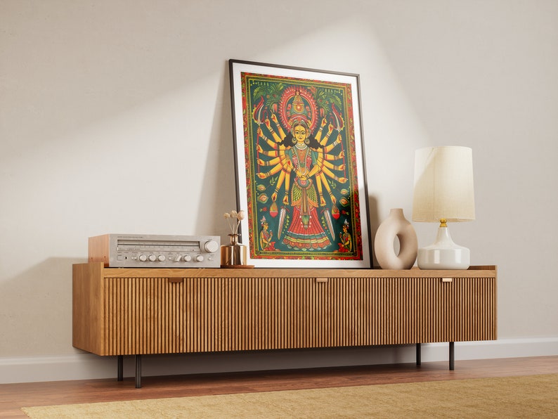 May include: A framed print of a colorful painting depicting a Hindu deity with multiple arms. The print is displayed on a wooden cabinet with a stereo system and a lamp.