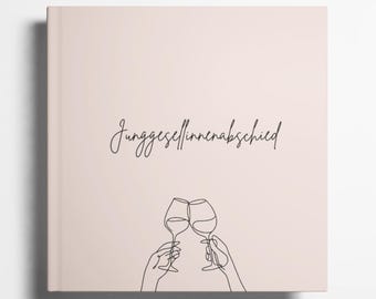 May include: A blush-colored square notebook with the German text "Junggesellinnenabschied" in a handwritten font. Below the text, a line drawing depicts two hands toasting with wine glasses.