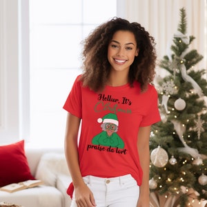 Könnte beinhalten: Rotes T-Shirt mit einem Cartoon-Bild einer Frau mit Weihnachtsmütze und Brille. Der Text auf dem Shirt lautet "Hellur. It's Christmas praise da lord."