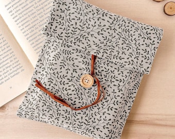 Könnte beinhalten: Eine graue Stofftasche mit einem schwarzen Blumenmuster und einem braunen Lederband zum Verschließen. Die Tasche hat einen Holzknopf und liegt auf einer Holzoberfläche.
