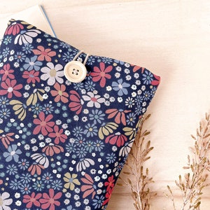 Può includere: Una pochette in tessuto blu con un motivo floreale e una chiusura a bottone bianco. La pochette è appoggiata su una superficie in legno chiaro.
