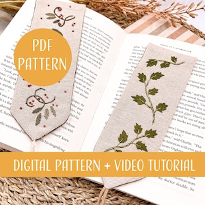 May include: Two digital embroidery patterns for bookmarks featuring a sprig of greenery with red berries and a single sprig of greenery. The patterns are displayed on a beige linen fabric. The text "PDF PATTERN" is displayed in a yellow circle on the left bookmark. The text "DIGITAL PATTERN + VIDEO TUTORIAL" is displayed in a yellow rectangle at the bottom of the image.