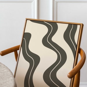 May include: A framed abstract print with a beige background and dark green wavy lines. The print is leaning against a wooden chair.