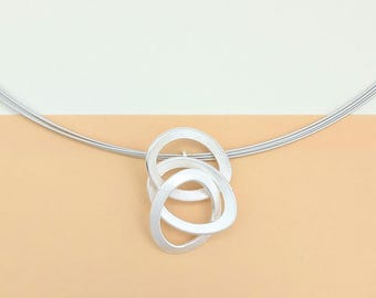 May include: A silver necklace with a pendant made of three interlocking circles. The circles are smooth and have a brushed finish.