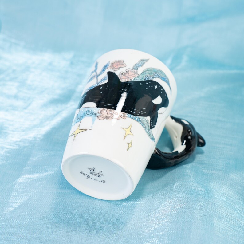 Puede incluir: Taza de cer&aacute;mica blanca con un dise&ntilde;o de orca en blanco y negro. La taza tiene un asa en forma de orca 3D. La taza est&aacute; decorada con un dise&ntilde;o floral y estrellas. El fondo de la taza est&aacute; marcado con el texto "2019.4.18"