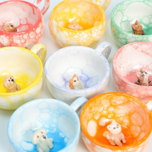 May include: A collection of colorful ceramic teacups with bubble-like patterns. Each cup features a miniature animal figurine inside, including a cat, dog, and rabbit.
