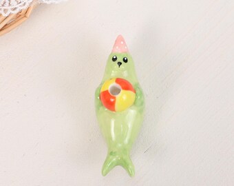 Playful Green Seal Cake Topper Hand Painted Ceramic Beach Ball Pink Party Hat Kawaii Whimsical Birthday Celebration Table Display