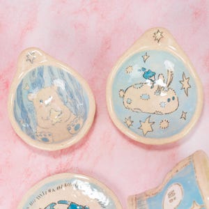 Può includere: Tre piatti in ceramica con smalto blu e bianco. Ogni piatto presenta un animale diverso: un orso, un coniglio e un uccello. I piatti sono decorati con stelle e hanno uno sfondo blu chiaro.