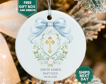 May include: A white ceramic Christmas ornament with a light blue bow and a gold cross design. The ornament includes the text "DAVID JAMES BAPTIZED 06.06.2025". The ornament is round and has a silver string for hanging.
