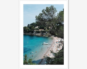 Puede incluir: Una vista panorámica de una playa con agua turquesa y una costa arenosa. La gente está nadando y tomando el sol en la playa. Hay barcos en el agua y una ladera verde exuberante en el fondo.
