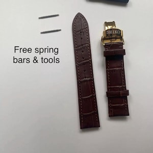May include: Brown leather watch strap with a gold buckle that says "SEIKO". The strap comes with two spring bars and a tool for changing the strap.