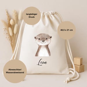 Op de afbeelding: Een cr&egrave;mekleurige trekkoordtas met een aquarel illustratie van een schattige otter. De tas meet 48,5 x 21 cm en heeft de naam "Leon" onder de otter gedrukt. De tas heeft een duurzame print en is wasbaar en waterafstotend.