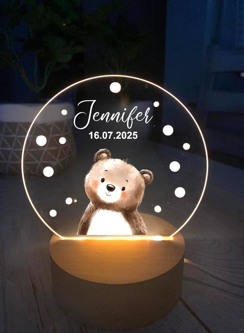 K&ouml;nnte beinhalten: Personalisiertes Nachtlicht mit einer B&auml;ren-Illustration. Die transparente Acrylplatte wird von einem warmen Licht beleuchtet, mit dem Namen "Jennifer" und dem Datum "16.07.2025". Der Sockel ist aus Holz.