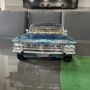 Könnte beinhalten: Ein tealfarbenes Cabrio-Modellauto mit Chromakzenten. Das Auto hat einen detaillierten Frontgrill, Scheinwerfer und eine beige Innenausstattung. Das Auto steht auf einer reflektierenden Oberfläche.