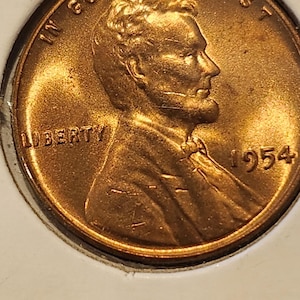 May include: A copper-colored 1954 Lincoln penny. The obverse features a profile of Abraham Lincoln, the word "LIBERTY," and the year "1954." The coin is in a protective holder.