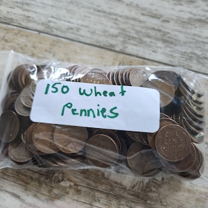 May include: A clear plastic bag filled with 150 wheat pennies. The label on the bag reads "150 Wheat Pennies" in green marker. The pennies are copper-colored and are visible through the transparent bag.