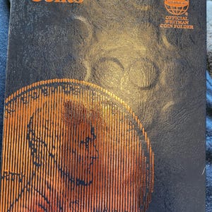 May include: A black coin folder with a gold embossed image of a coin and the text "Cents" on the front. The folder is labeled "Official Whitman Coin Folder" and has the Whitman logo with a globe design. The number 9041 is printed on the bottom right corner.