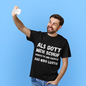 Könnte beinhalten: Ein schwarzes T-Shirt mit weißem Text, der "Als Gott mich schuf grinste er und dachte Das wird lustig" lautet.