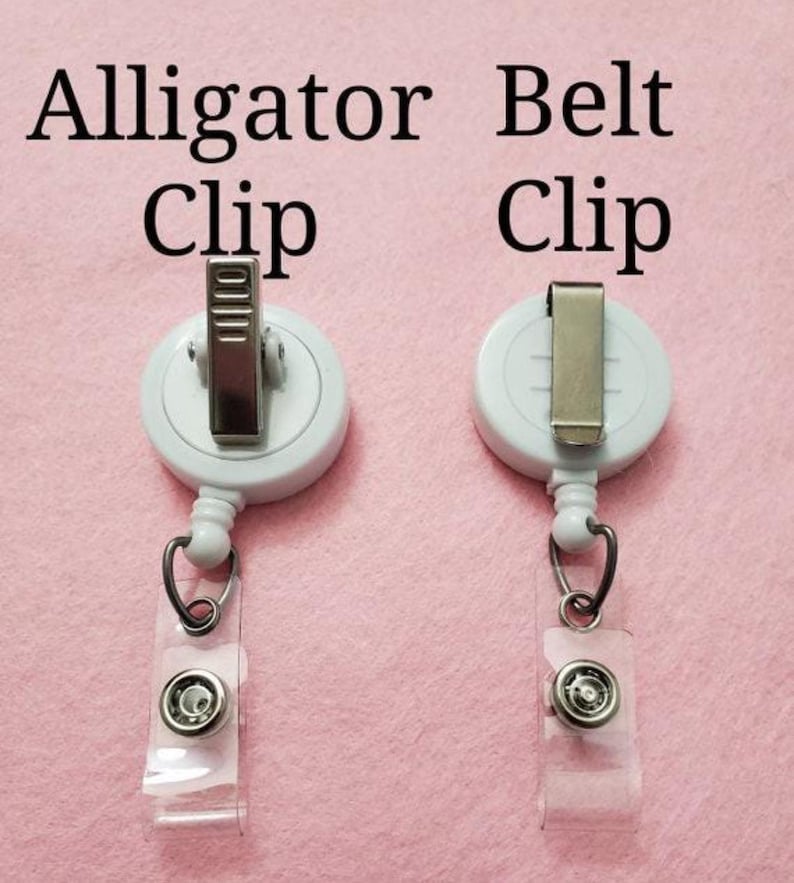 Puede incluir: Dos clips de carrete de insignia blancos con diferentes estilos de clip met&aacute;lico. El clip izquierdo es un clip de cocodrilo, y el clip derecho es un clip de cintur&oacute;n. Ambos tienen una correa de pl&aacute;stico transparente con cierre a presi&oacute;n y un anillo de metal.