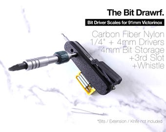 May include: Black carbon fiber nylon bit driver scales for 91mm Victorinox, featuring 1/4 inch and 4mm drivers, 4mm bit storage, a third slot, and a whistle. The text reads: The Bit Drawrf. Bit Driver Scales for 91mm Victorinox.