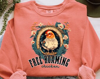 May include: A coral colored sweatshirt with a graphic of a chicken in a floral frame. The text "FREE ROAMING chicken" is printed below the image.