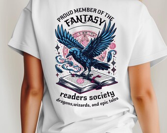 May include: White t-shirt with a graphic featuring a blue raven perched on an open book. The text reads "PROUD MEMBER OF THE FANTASY READERS SOCIETY" with additional text about dragons, wizards, and epic tales. The design is detailed and colorful.