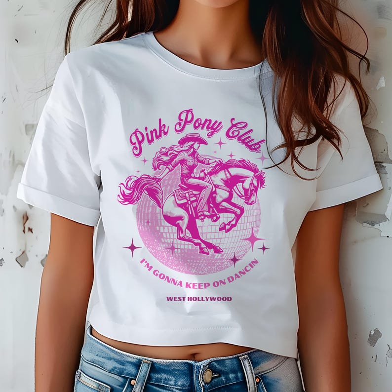 May include: White cropped t-shirt with a pink graphic of a woman riding a horse in front of a disco ball. The graphic says "Pink Pony Club" and "I'm gonna keep on dancin' West Hollywood".
