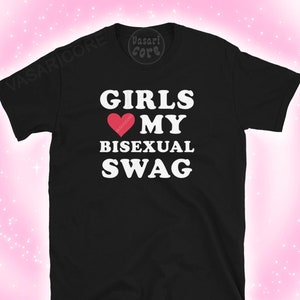 May include: Black t-shirt with white text that reads "Girls love my bisexual swag". A red heart with the word "bisexual" inside is above the word "my".