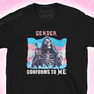 May include: Black t-shirt featuring a graphic of a skeleton holding a glass, with the text "GENDER CONFORMS TO ME". The skeleton is set against a transgender flag background. The shirt has short sleeves and a crew neck.