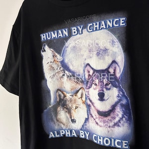 May include: Black t-shirt with a graphic of three wolves howling at the moon. The text "HUMAN BY CHANCE ALPHA BY CHOICE" is printed on the shirt.
