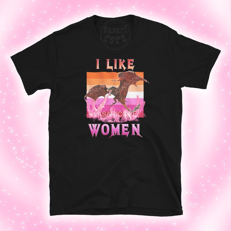 K&ouml;nnte beinhalten: Schwarzes T-Shirt mit einem Grafikdruck von zwei k&auml;mpfenden Drachen vor einer pinkfarbenen, orangen und wei&szlig;en lesbischen Pride-Flagge. Der Text "ICH MAG FRAUEN" befindet sich unter dem Grafikdruck.