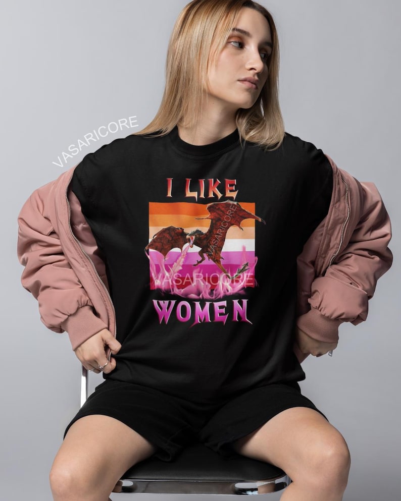 K&ouml;nnte beinhalten: Schwarzes T-Shirt mit einem Grafikdruck eines Drachen und dem Text "Ich mag Frauen" in rosa und orangefarbener Schrift.