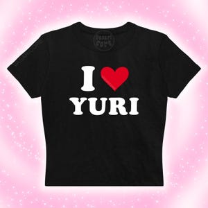 May include: Black crop top with the text "I ♥ YURI" in white, with a red heart replacing the word "love". The shirt has short sleeves and a crew neck. The brand name "VASARICORE" is printed on the shirt.