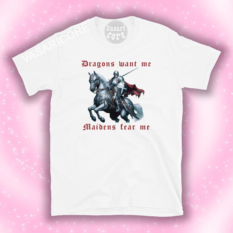 Może przedstawiać: Biała koszulka z nadrukiem przedstawiającym rycerza na białym koniu. Tekst "Dragons want me" i "Maidens fear me" jest nadrukowany na koszulce na czerwono.