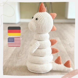 May include: A white crocheted dinosaur toy with orange spikes. The dinosaur is a stacking toy with five rings.