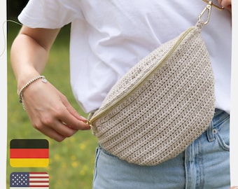 May include: A beige crocheted fanny pack with a gold zipper. The bag is worn around the waist of a person wearing a white t-shirt and blue jeans.