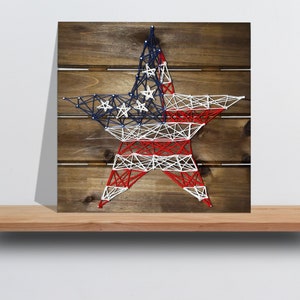 May include: A red, white, and blue string art star on a wooden background. The star is made of string wrapped around nails hammered into the wood.