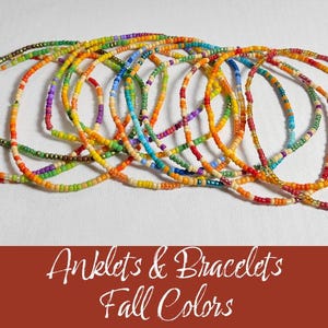 May include: A collection of colorful beaded anklets and bracelets in fall colors. The bracelets are made with small, colorful beads and are arranged in a pile.