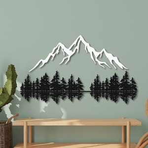 May include: Black metal wall art depicting a mountain range with a reflection of trees in a lake. The mountain peaks are white and the trees are black.
