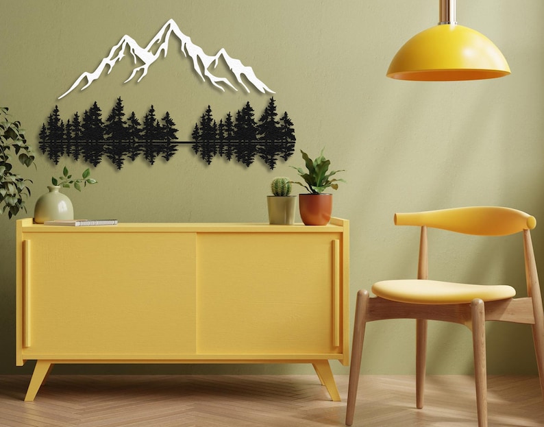 May include: Black metal wall art depicting a mountain range with trees reflected in a lake. The art is mounted on a light green wall above a yellow cabinet and a yellow chair.