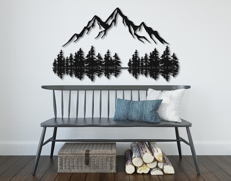 May include: Black metal wall art depicting a mountain range with a reflection of the mountains in a lake below. The mountains are silhouetted against a white background. The art is displayed on a white wall above a gray bench with pillows.