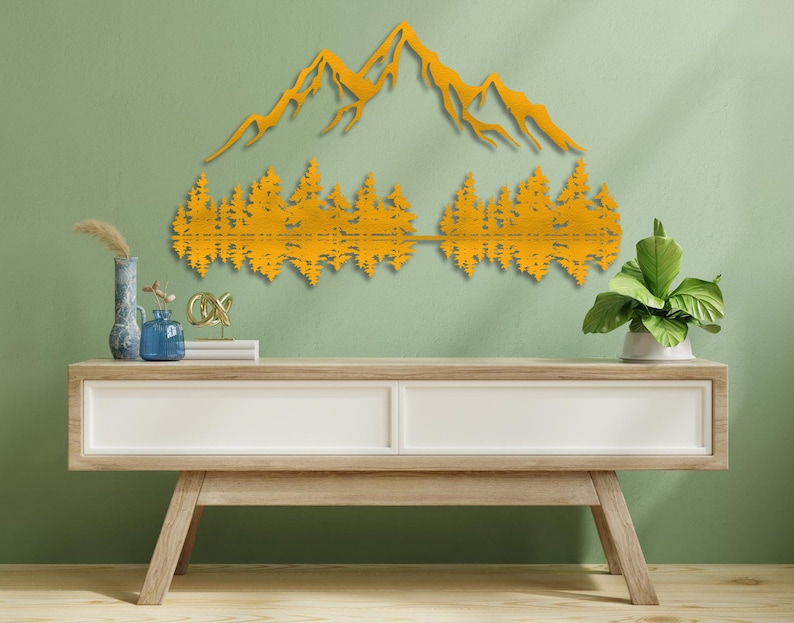 May include: A gold metal wall art sculpture depicting a mountain range with trees reflected in a lake. The sculpture is mounted on a light green wall above a light wood console table.